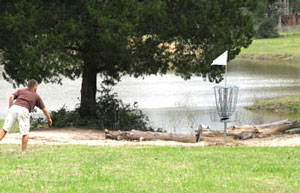 Man throwing disc into to disc golf basket